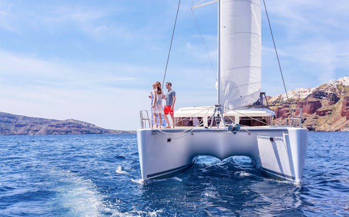 Catamaran sailing near Santorini cliffs on a semi-private day cruise.