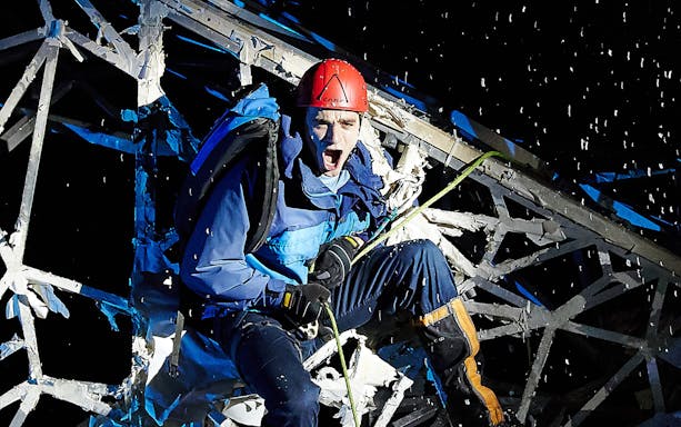 Climber in red helmet scaling icy structure at night, Touching The Void experience.