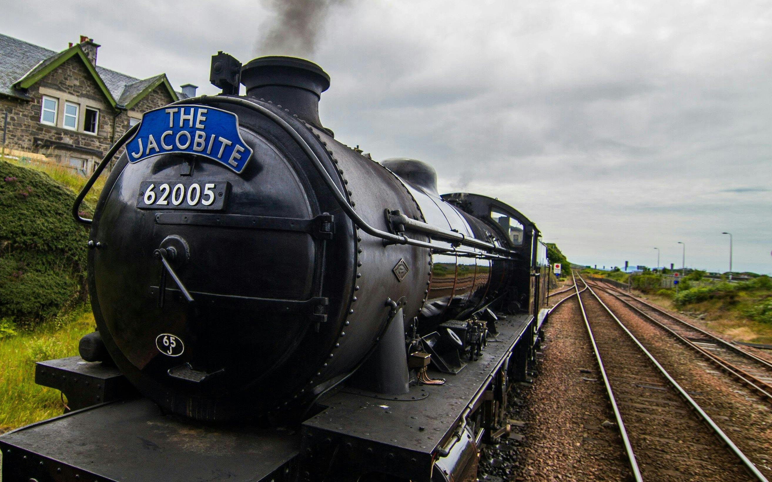 Steam train "The Jacobite" traveling on railway tracks in the countryside.