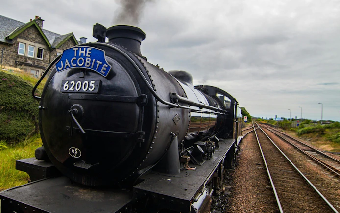 Steam train "The Jacobite" traveling on railway tracks in the countryside.