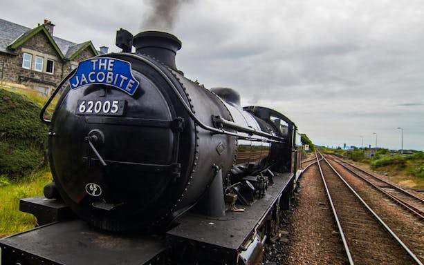 Steam train "The Jacobite" traveling on railway tracks in the countryside.