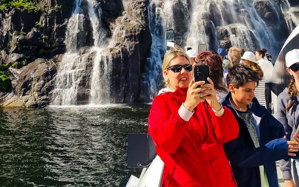 Guests taking photos on Lysefjord cruise near waterfall in Stavanger.