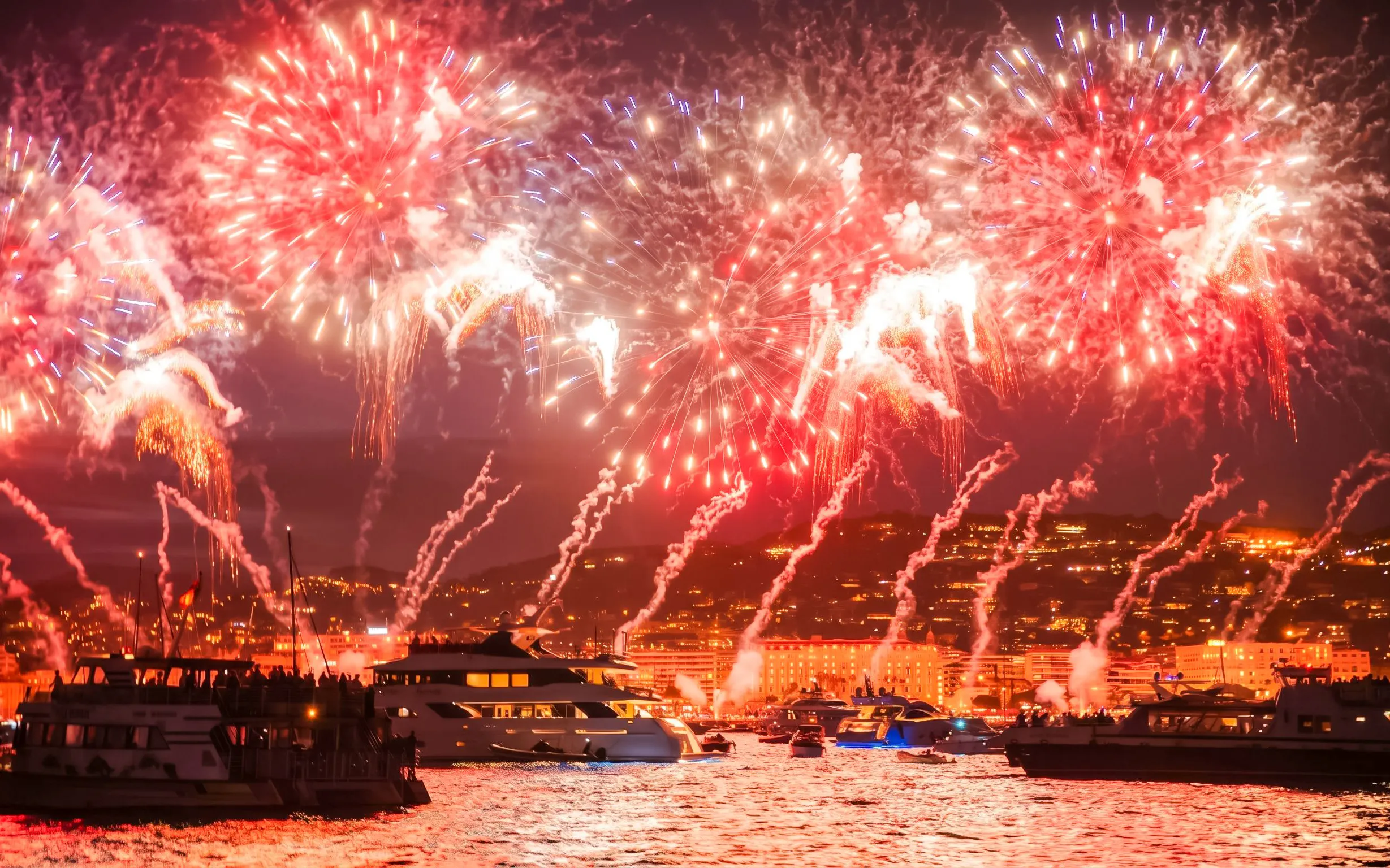 Boats on French Riviera with fireworks illuminating the night sky.