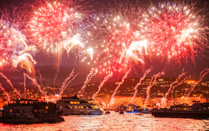 Boats on French Riviera with fireworks illuminating the night sky.