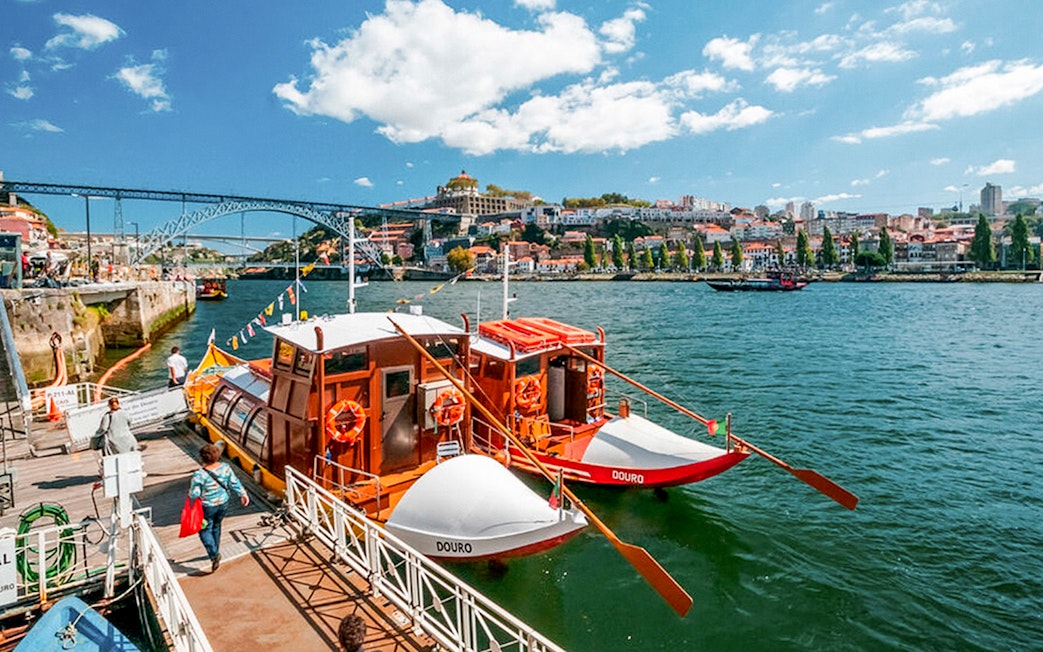 Tourists boarding a boat for a Douro River cruise in Porto, with the Dom Luís I Bridge in the background.