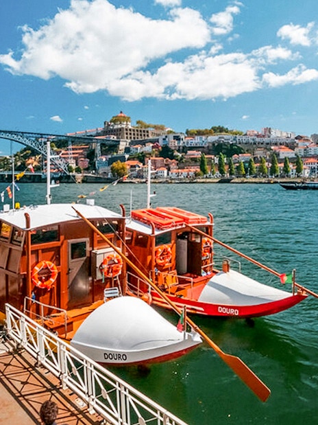 Tourists boarding a boat for a Douro River cruise in Porto, with the Dom Luís I Bridge in the background.