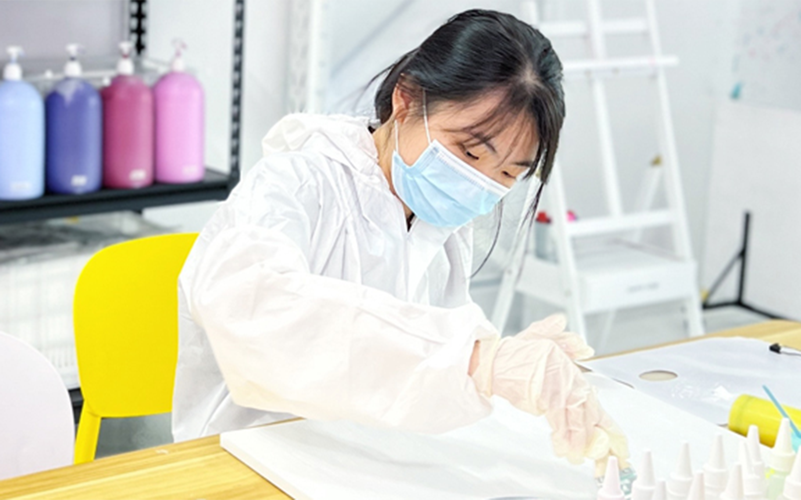 Person mixing colors at Balloon Splatter Art Workshop with paint bottles in background.
