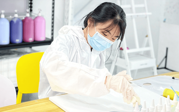 Person mixing colors at Balloon Splatter Art Workshop with paint bottles in background.