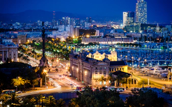 Barcelona cityscape at night with Columbus Monument and Port Vell marina.