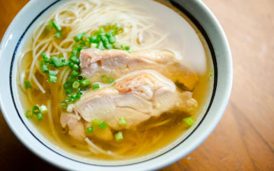 Bowl of ramen in broth with sliced chicken and green onions.