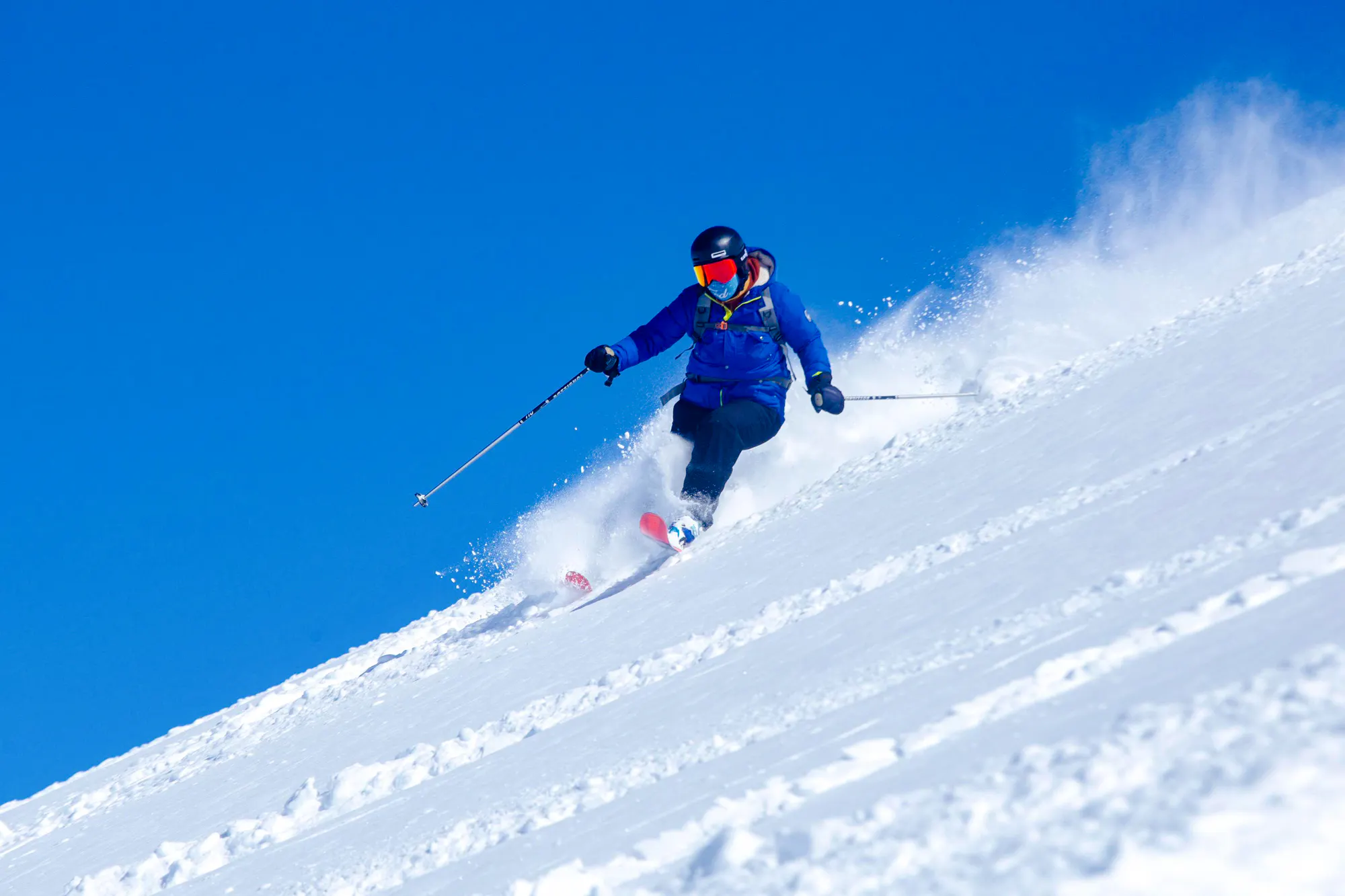 Skier descending snowy slope in Farellones, Santiago, with clear blue sky.