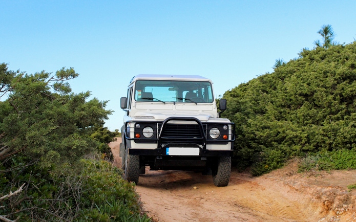 4x4 Jeep on a dirt path during Cape Espichel tour, surrounded by greenery.