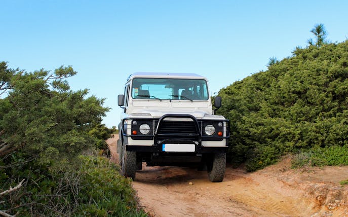 4x4 Jeep on a dirt path during Cape Espichel tour, surrounded by greenery.