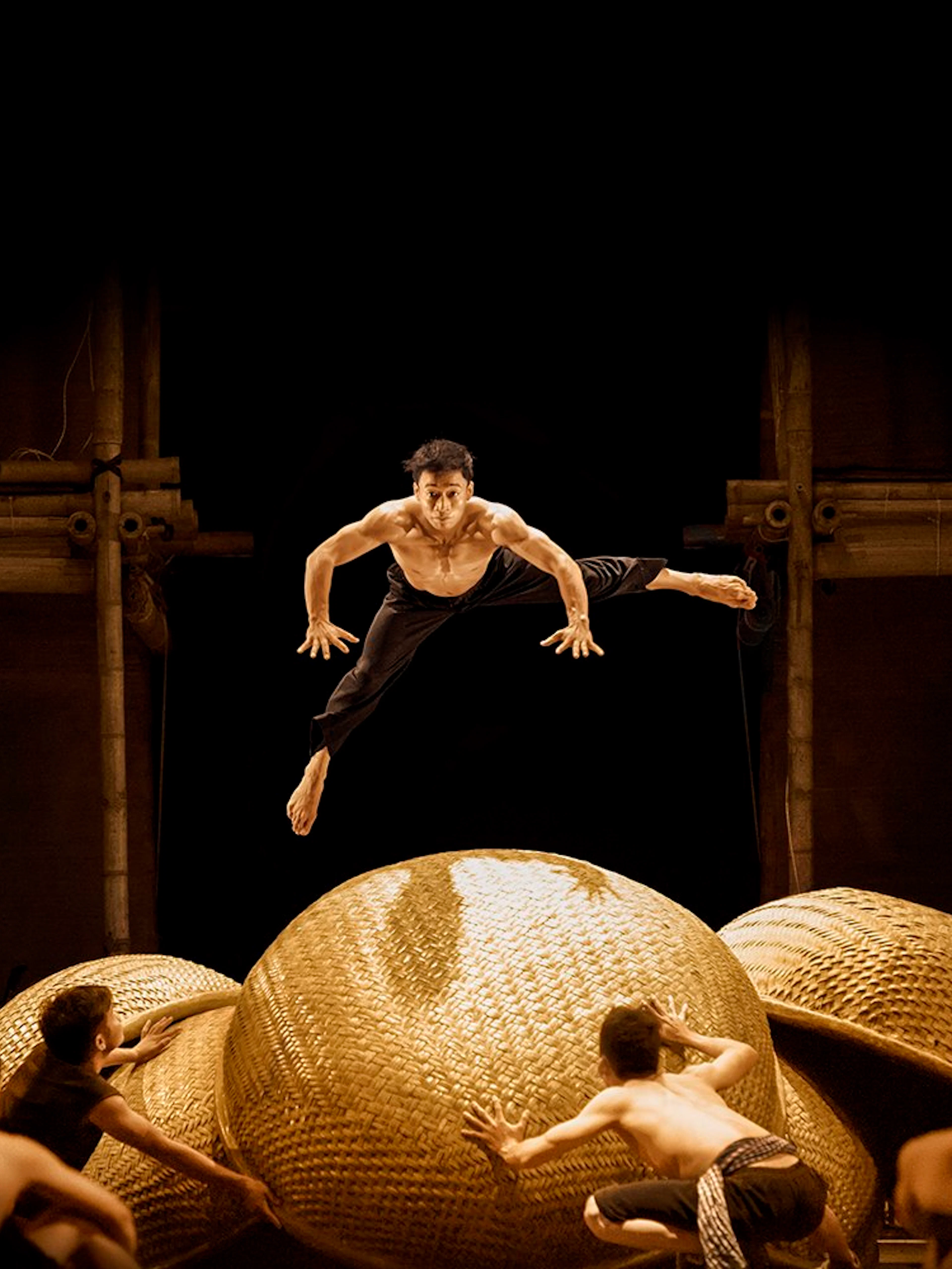 Performers leaping on stage at AO SHOW with bamboo props.