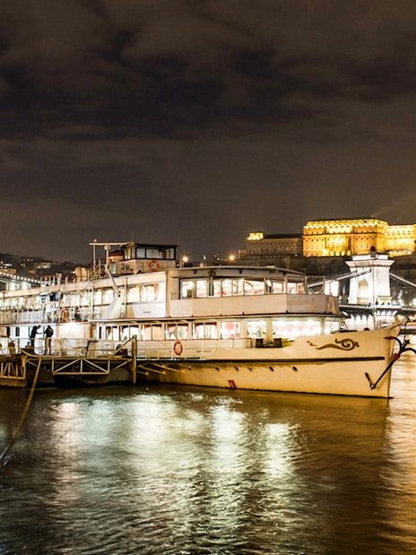 Sightseeing cruise on the Danube River with Budapest's Chain Bridge and Buda Castle illuminated at night.