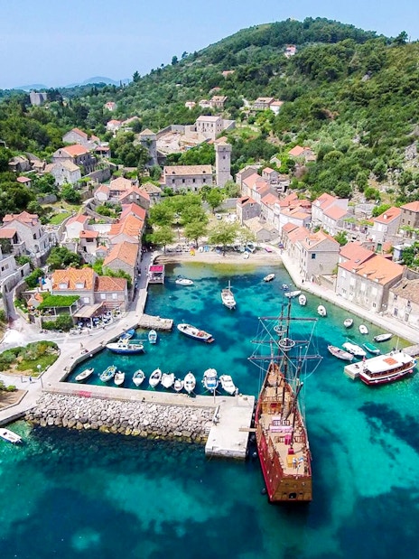 Ship docked at Elaphiti Islands harbor with surrounding village and hills.