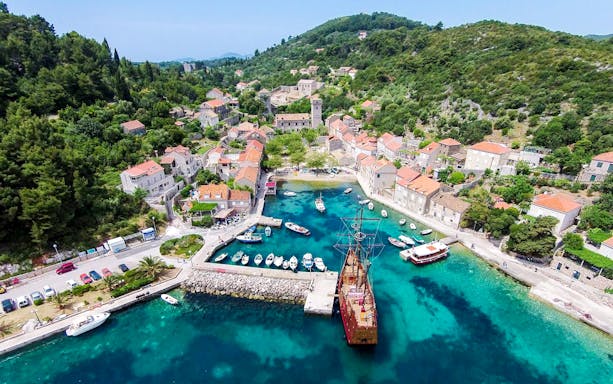 Ship docked at Elaphiti Islands harbor with surrounding village and hills.