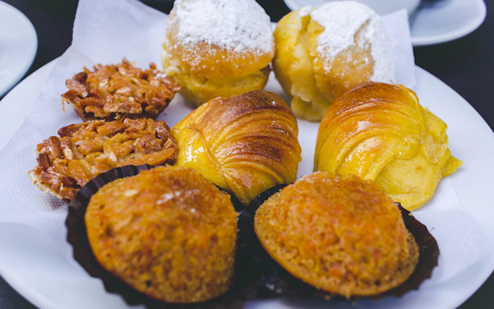 Portuguese pastries including almond tarts and sugar-dusted rolls on a plate.
