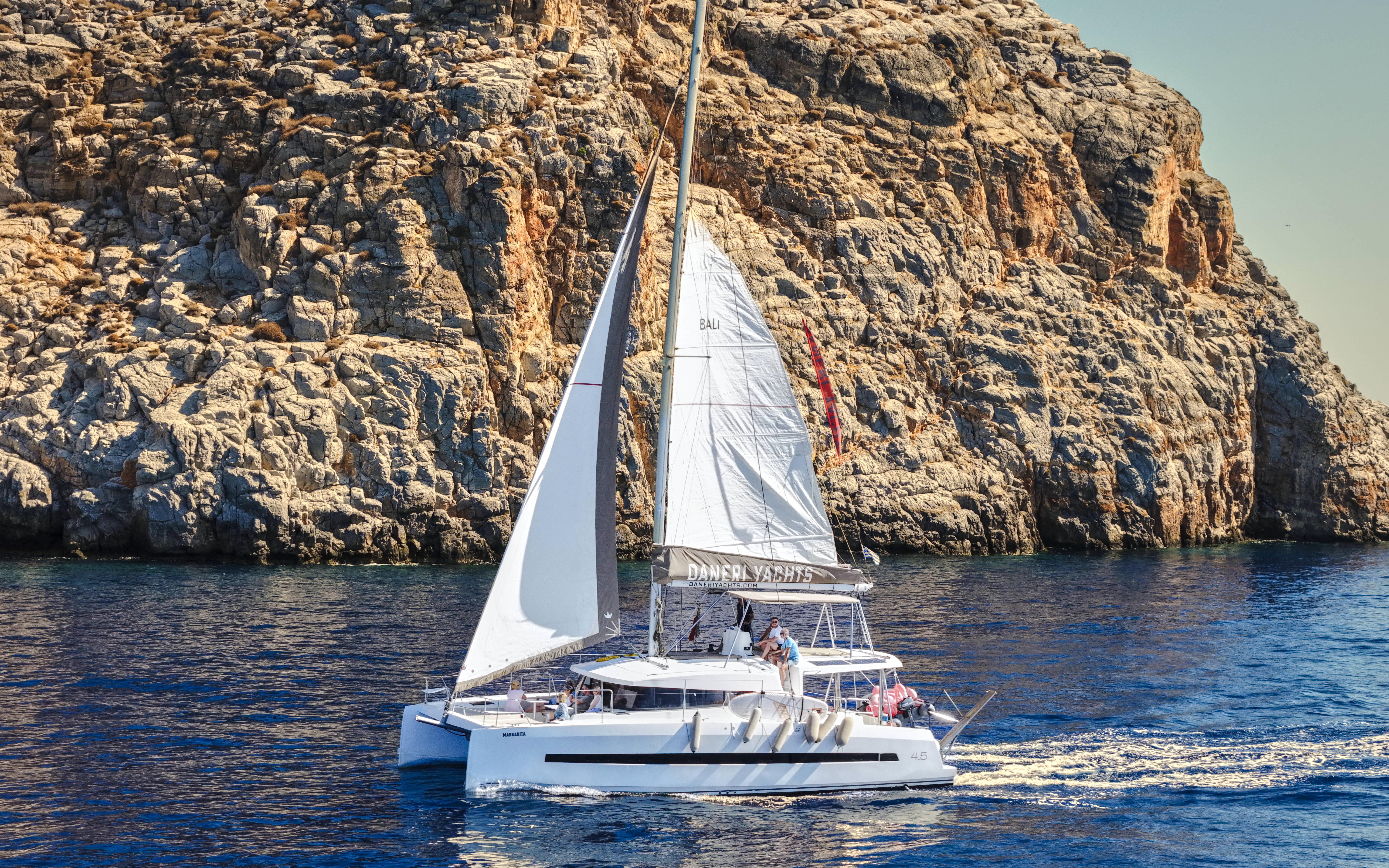 Catamaran sailing near rocky cliffs on Dia Island during a day cruise.