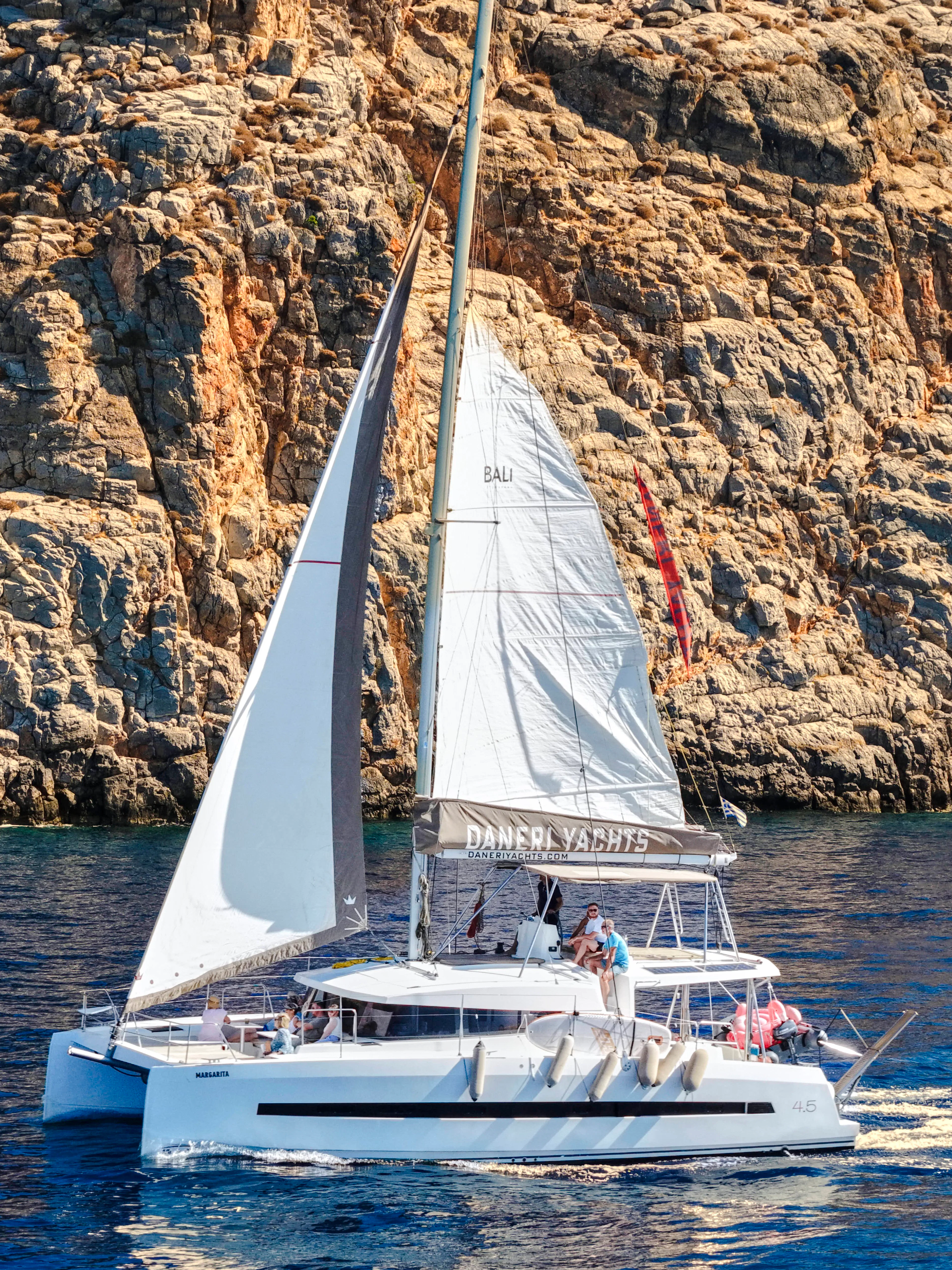 Catamaran sailing near rocky cliffs on Dia Island during a day cruise.
