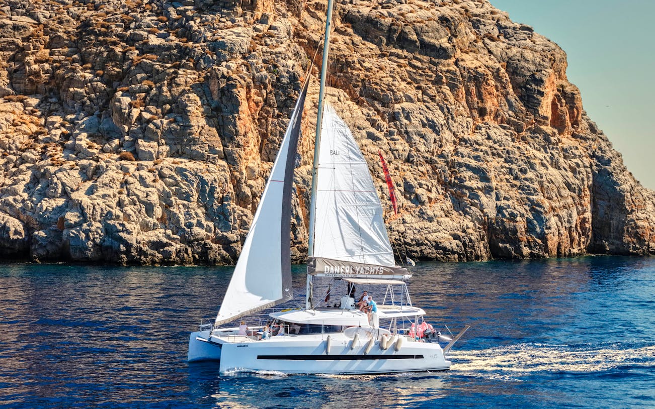 Catamaran sailing near rocky cliffs on Dia Island during a day cruise.