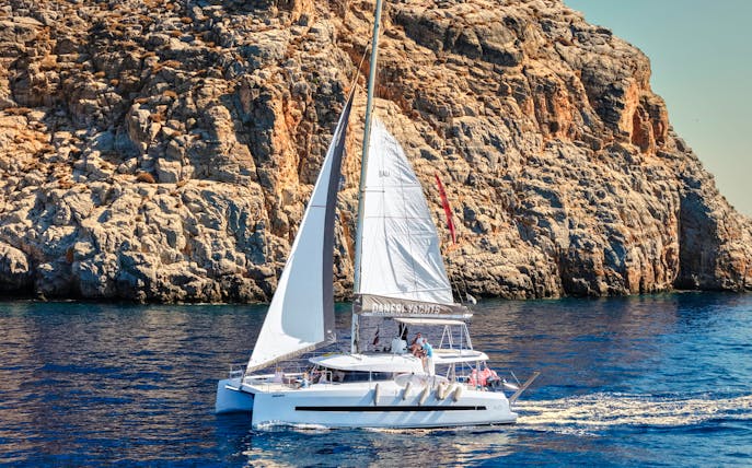 Catamaran sailing near rocky cliffs on Dia Island during a day cruise.
