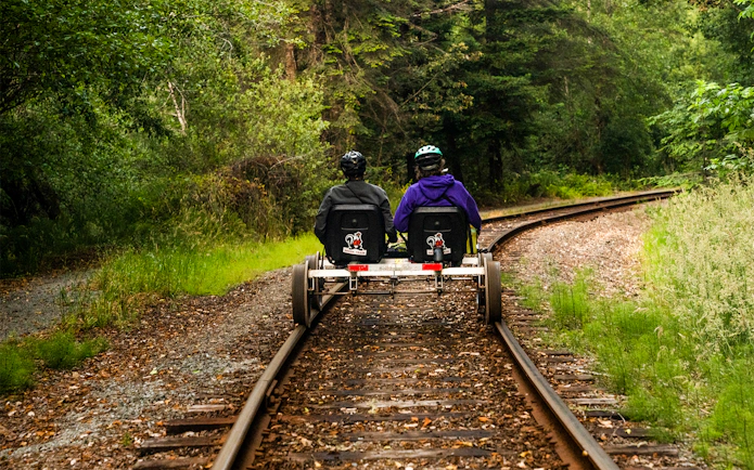 Two people riding railbikes on a forested track towards Glen Blair Bar.