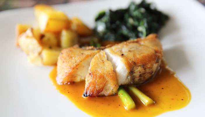 Sea bass fillet steak with asparagus, potatoes, and greens on a white plate.