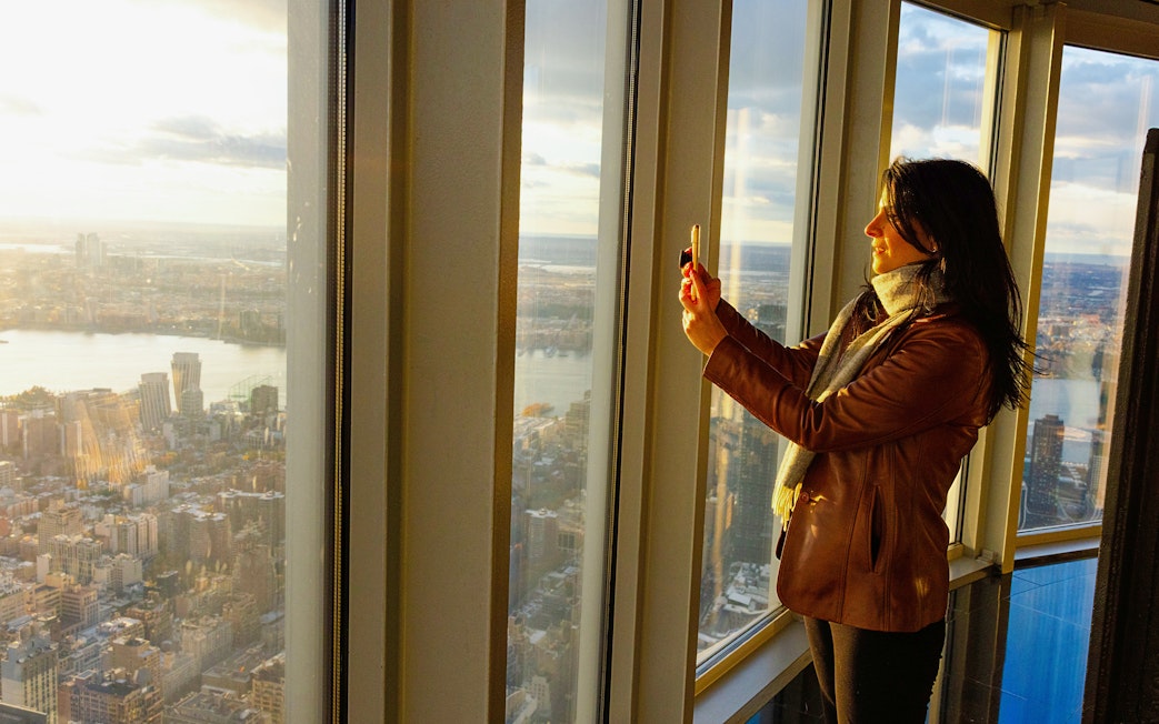 Guest taking photo at Empire State Building observatory with city view.