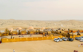 Desert camp with domed tents and parked SUVs in Abu Dhabi for a private safari and sandboarding experience.