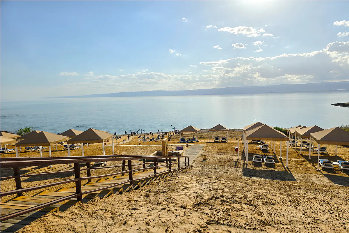 Dead Sea beach with sunshades and lounge chairs, view from Amman half-day trip.