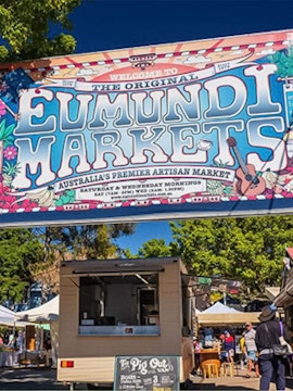 Eumundi Markets entrance sign with food stalls and visitors in Queensland, Australia.