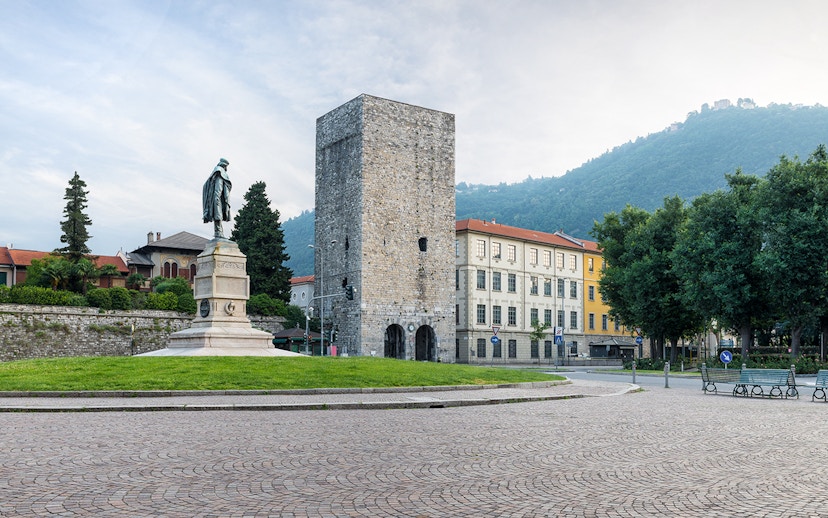 Porta Torre in Como, Italy, with a statue and surrounding buildings.