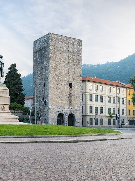 Porta Torre in Como, Italy, with a statue and surrounding buildings.