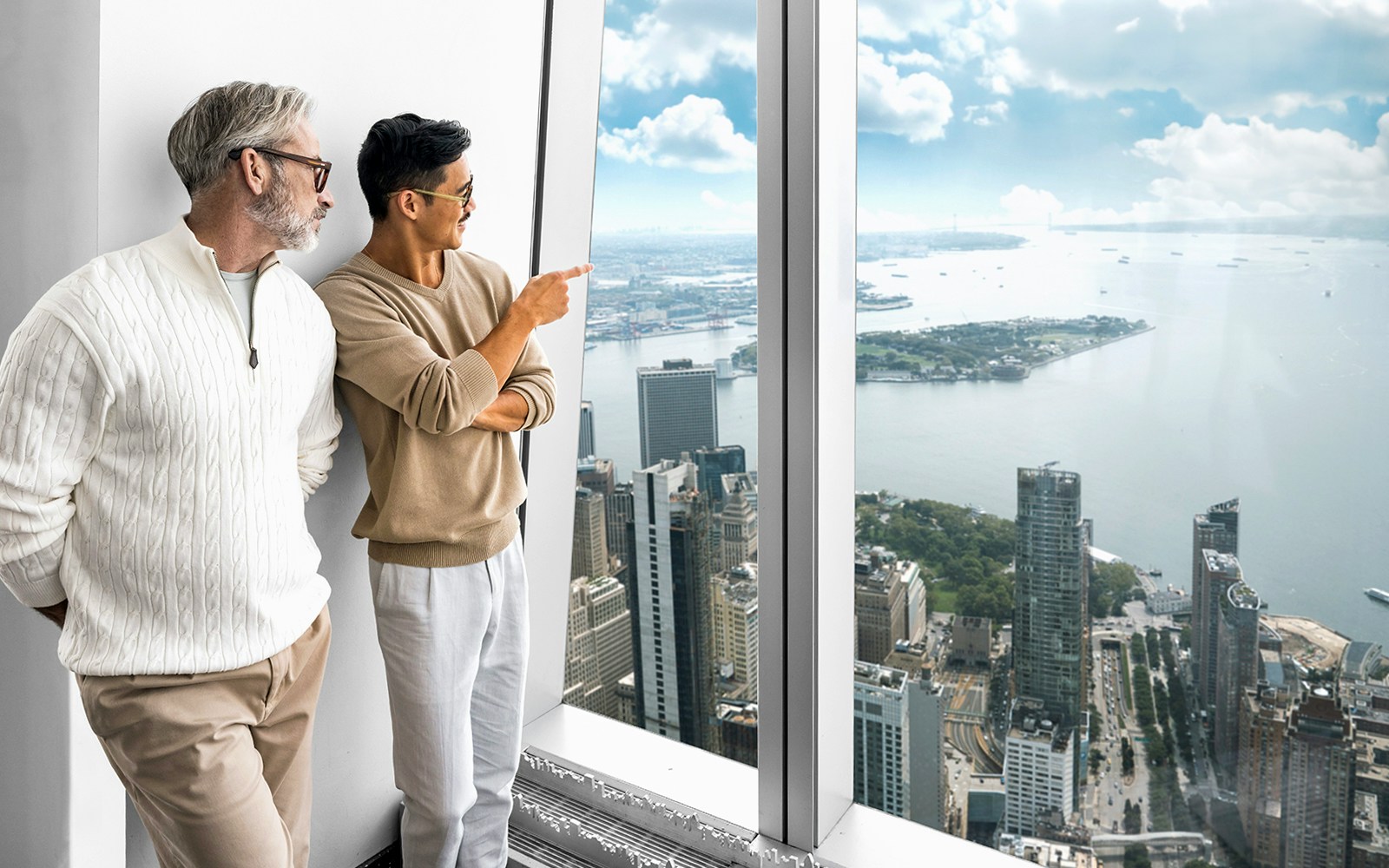 Visitors enjoying the view from One World Observatory, overlooking New York City skyline and harbor.