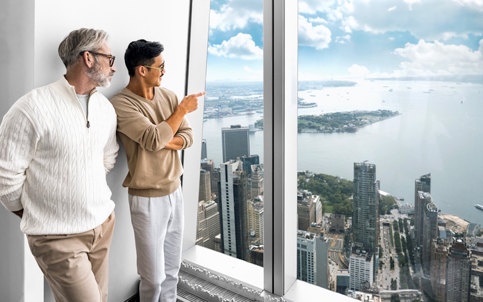 Visitors enjoying the view from One World Observatory, overlooking New York City skyline and harbor.