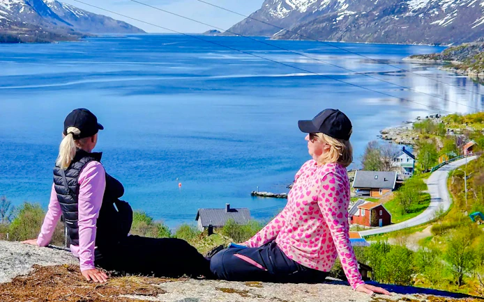 Two people sitting on a hill overlooking Sommarøy Fjord, Tromsø, with scenic mountain views.