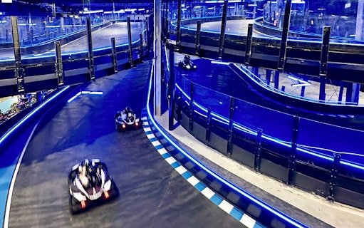 Go-karts racing on an indoor track with blue neon lights, part of Combo: HyperDrive and UltraGolf experience.