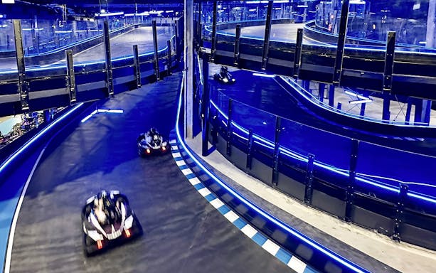 Go-karts racing on an indoor track with blue neon lights, part of Combo: HyperDrive and UltraGolf experience.