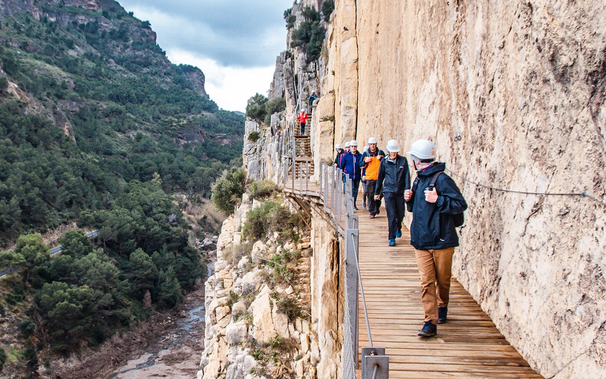 Trekkers walking along a narrow path on a guided tour of Caminito del Rey, Spain.