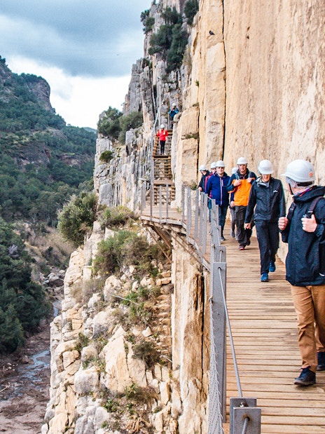 Trekkers walking along a narrow path on a guided tour of Caminito del Rey, Spain.