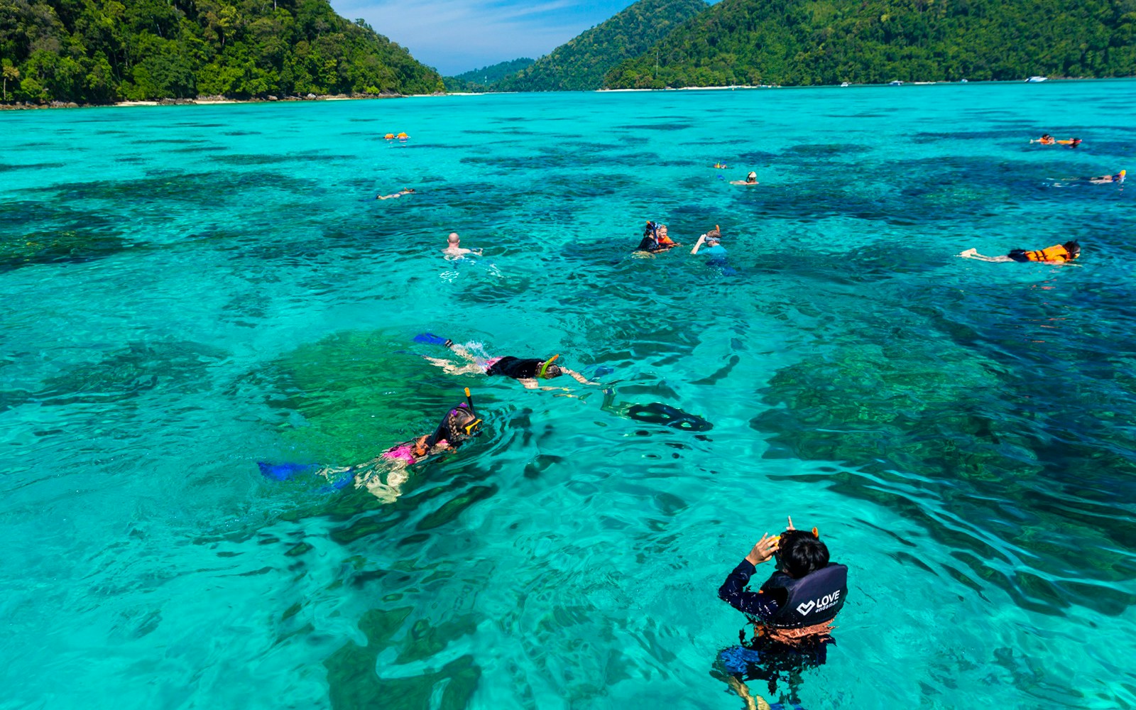 Snorkelers exploring clear waters near Surin Island, Thailand, with lush green hills in the background.