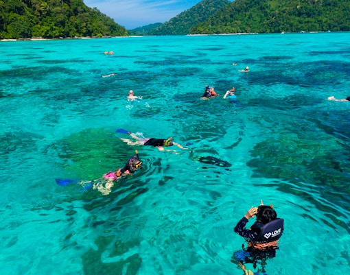 Snorkelers exploring clear waters near Surin Island, Thailand, with lush green hills in the background.
