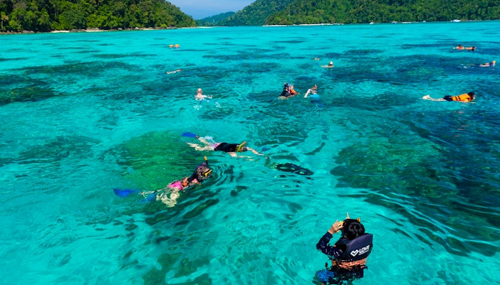 Snorkelers exploring clear waters near Surin Island, Thailand, with lush green hills in the background.