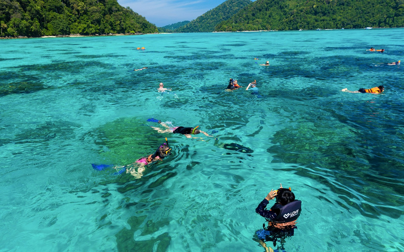 Snorkelers exploring clear waters near Surin Island, Thailand, with lush green hills in the background.