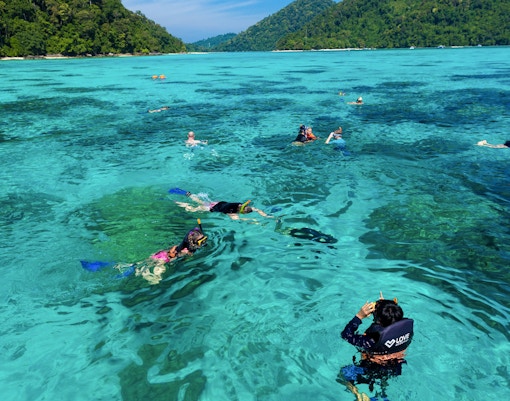 Snorkelers exploring clear waters near Surin Island, Thailand, with lush green hills in the background.