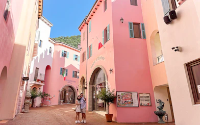 Couple in narrow cobblestone street between pink buildings at Italian Village, South Korea.