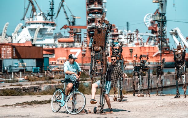 Man on bike and another interacting with metal sculptures at Gdansk shipyard during private bike tour.