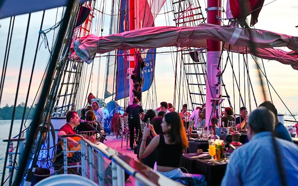 Guests dining on the deck of The Royal Albatross during a sunset cruise.