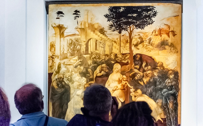 Visitors viewing Leonardo Da Vinci's "Adoration of the Magi" painting in a museum.